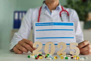 Doctor displaying health insurance claim form alongside pills and the year 2025 on a desk