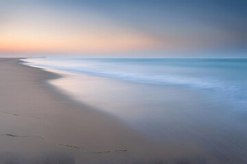 Empty Beach at Dawn with Gentle Waves and Misty Horizon in Soft Blue Light, Evoking Solitude and Reflection, sunrise on the beach