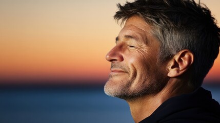 Man smiling at sunset by the sea, conveying peace and contentment.