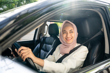 Asian muslim business women getting new car. She very happy and excited. Smiling female islamic driving vehicle on the road on a bright day with sun light. Business woman buying driving new car