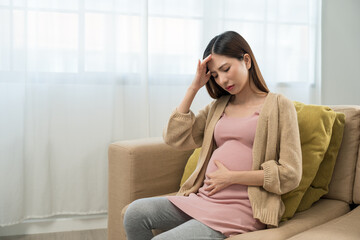 Young pregnant woman suffering from headache and abdominal pain alone at home, tired and stressed...