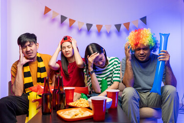 Sports fans feel sad when the team they support loses. Group of asian friends man and woman watching cheering football match on TV at home. Eating snack and drinking beer.