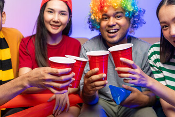 Group of asian friends man and woman watching cheering football match on TV at home. Eating snack...