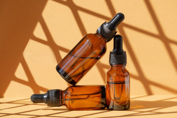 Three bottles serum in glass package made of amber glass with dropper lids. Brown background with rays of sunlight and shadows. Concept of rejuvenation and body care