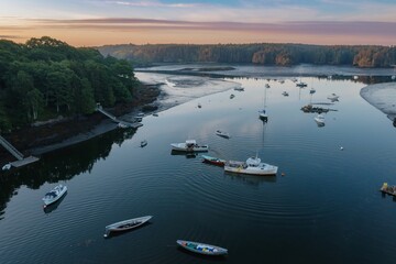 Boats moored in the calm Branch estuary during low tide at sunrise. The estuary is surrounded by forest, Phippsburg, Maine, United States.