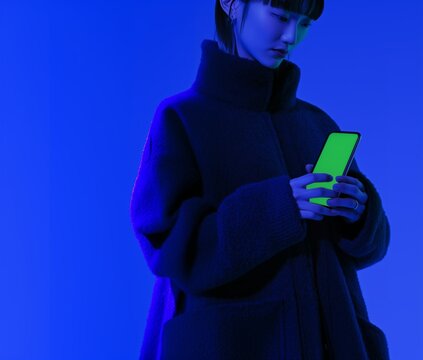 Young woman in a cozy coat interacting with a smartphone under vibrant blue and green lighting in an indoor space