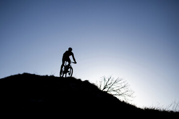 A man rides a bicycle down the mountain. Photo against the sun, silhouette against a blue sky.