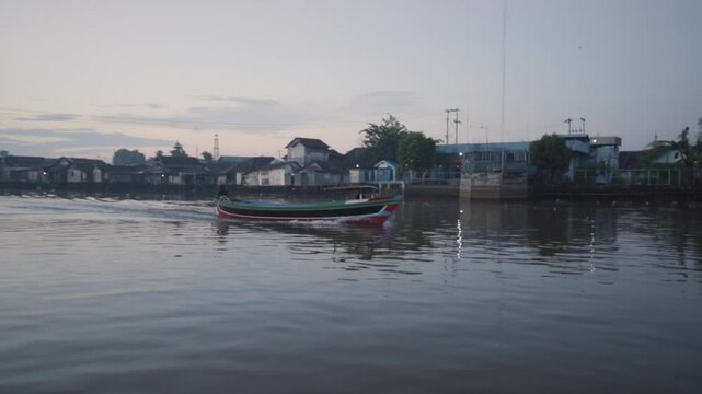 Colorful Motorboat Speeds Through Calm Urban Waters at Dusk, Banjarmasin