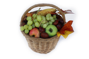 Various fresh autumnal fruits in a wicker basket with orange and yellow leaves. Grapes, apples,...
