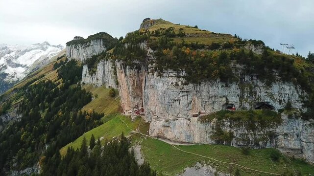 Pull our aerial shot of the Aescher cliff restaurant nestled into the rock face in autumn, the Ebenalp mountain with the Wildkirchli caves, Appenzell, Switzerland