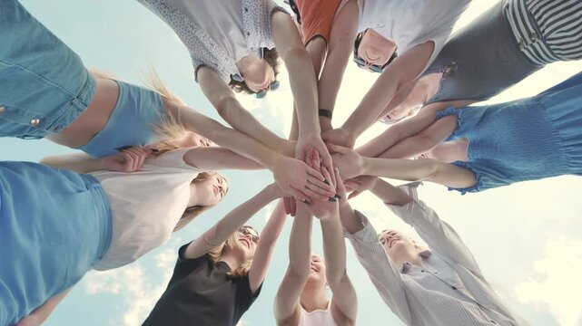 Group of young friends are standing in a circle joining hands together outdoors on a sunny day.