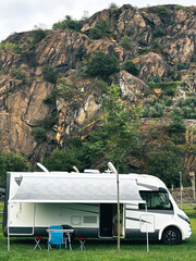 Modern motorhome parked in a peaceful meadow with stunning mountain views and open veranda setup, ideal for alternative travel and embracing the vanlife lifestyle