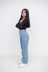 A pretty southeast asian woman, dressed casually in a black long-sleeve crop top with a square neckline, light-wash ripped jeans, and white sneakers. Isolated on a white background.