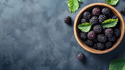 Farm-fresh blackberries displayed in a wooden bowl on a rustic grey table from a top view perspective. Enjoy the organic ripe berry with ample copy space for your projects.
