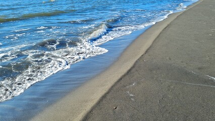 Sea waves roll onto the sandy shore, the glare of the sun plays on the water