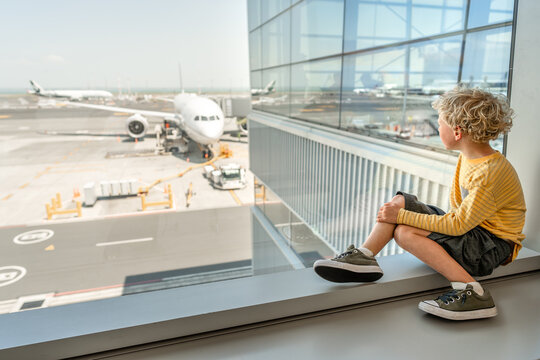 Young curly haired child looking at airplane from airport