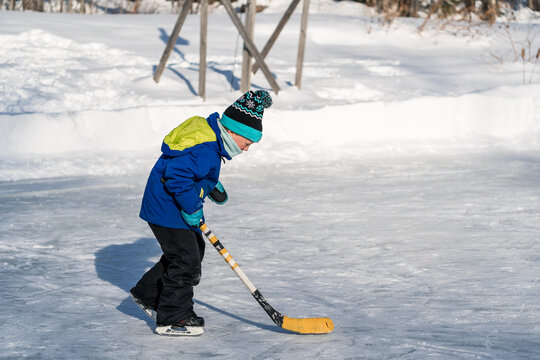 Young child ice skating outdoors with hockey stick