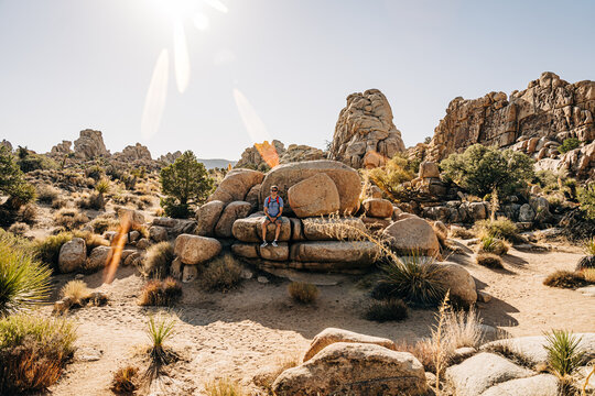 Man seated on large desert rock formation under sunny sky