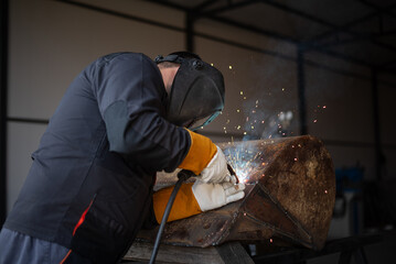 Industrial worker welding metal with sparks flying in workshop