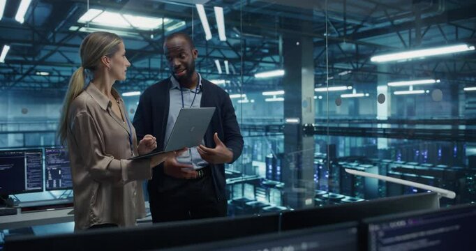 Male Cloud Architect and Female Database Engineer Review Data Storage Protocols on a Shared Laptop in a Data Center. Team Strategizing Ways to Improve Service for Enterprise Clients