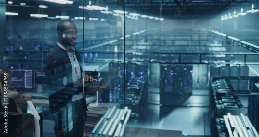 Poster African Male Network Administrator Standing in a High-Tech Data Center, Optimizing Server Configurations on a Laptop Computer to Improve Performance for a Major Corporate Client