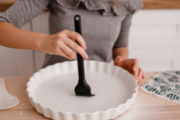 A teenage girl prepares an apple pie in the kitchen, buttering a baking mold