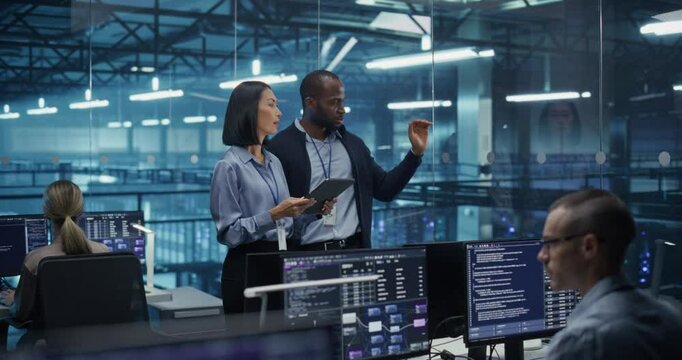 Male DevOps Engineer and Female IT Consultant Using a Tablet Computer, Standing in an Office Above the Rows of Servers in a Data Center, Developing Automation Scripts for Artificial Intelligence