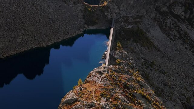 Aerial view of the Enel weir at Lago Pirola, nestled in the scenic landscape of Valmalenco, Lombardy. Orbit Motion