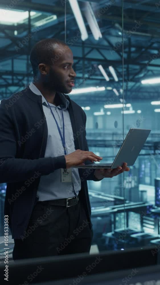 Fototapete Vertical Screen: Black Male Software Developer Analyze System Performance Metrics on a Laptop Inside a Modern Data Center. Young Manager Ensuring Efficient Operations for Critical Infrastructure