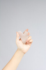 Female model hands with pink rose quartz jade guasha scraper on white background. Spa body care tool. Beauty care gua sha stone scraper.