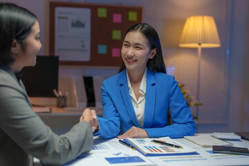 Two Asian businesswomen come up with an idea. Discuss investment projects and strategic planning with information via various documents and files. On a laptop computer at modern office.