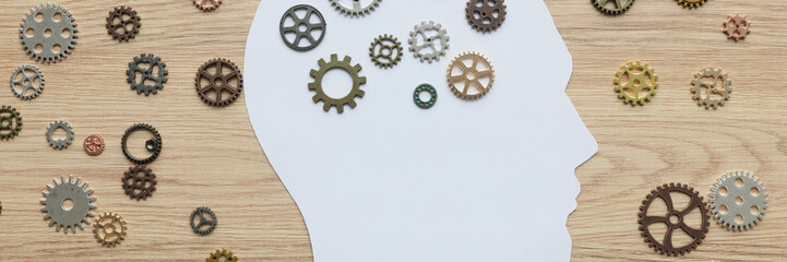 Paper human head with small cogwheels on wooden surface