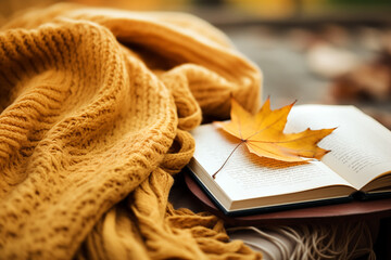 Autumn leaves. An open book near a knitted blanket with a fallen leaf close up.