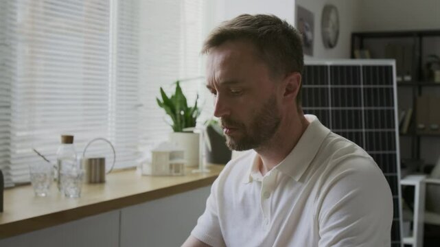 Bearded Caucasian man wearing white polo shirt typing on computer at workplace in modern sustainable office