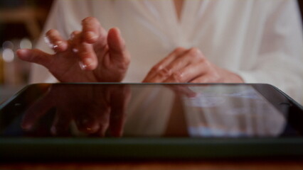 An old woman scrolls photos on a tablet in a cafe. Senior female looks at photos in a restaurant, touches the touch screen with her fingers. The concept of modern technologies.