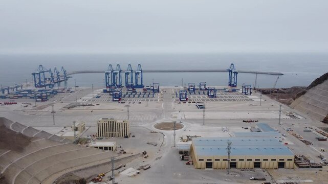 Aerial shot of a new Megaport under construction in the city of Chancay, Peru. Drone slowly orbits around. Many blue cranes can be seen on the edge of the harbor and behing the ocean horizon.