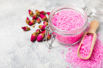 Sea salt for bath with aroma and rose flowers on textured wooden background. Pink sea salt. Spa treatments. Natural salt with herbs and essential oils. skincare concept. Meso for text. Copy space