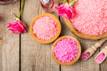 Sea salt for bath with aroma and rose flowers on textured wooden background. Pink sea salt. Spa treatments. Natural salt with herbs and essential oils. skincare concept. Meso for text. Copy space