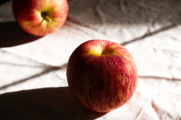 Apples placed on beige tablecloth under sunlight with noise texture.  Noise image of still-life red apple and shadow. Fresh fruit, art, abstract, and cotton cloth concept. Two apples in rustic kitchen