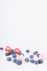 Blueberries and colorful flowers scattered on a white surface, showcasing a beautiful blend of nature’s colors and textures in a simple composition