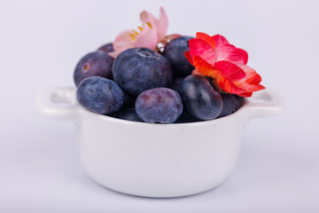 Detailed view of blueberries in a bowl with red and pink flowers on a white background, showcasing vibrant colors in a refreshing scene