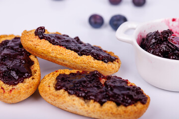 Detailed view of blueberry jam on toast and a jam jar on a clean white background, perfect for breakfast, snacks, or food presentations
