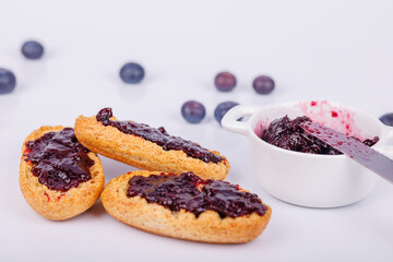 Toasts spread with blueberry jam and a jar on a white backdrop, highlighting the texture and color of this delicious morning treat