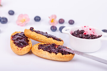 Detailed close-up of toast with blueberry jam and a jar of jam on a white background, capturing texture and vibrant color