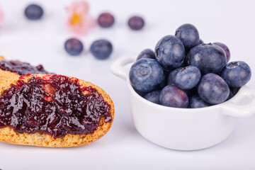Toast topped with fresh blueberry jam alongside a jar, set on a white background, featuring rich color and texture details