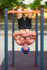 Fototapeta premium Young man wearing headphones hanging upside down from horizontal bar