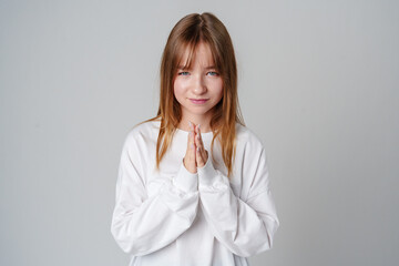 Young girl with long hair in a white sweater, smiling and posing with hands together in a friendly gesture