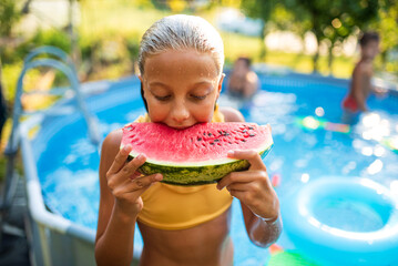 Girl eating watermelon by the swimming pool on a sunny day