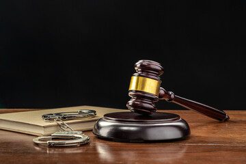 Judge's gavel and a set of handcuffs on a dark colored wooden table welly lit with black background