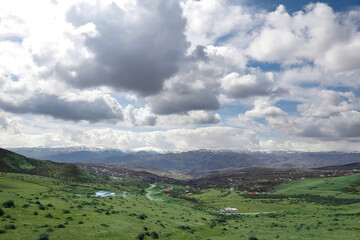 Fototapeta premium A village on the slopes of the mountain, cloudy sky, meadows and trees